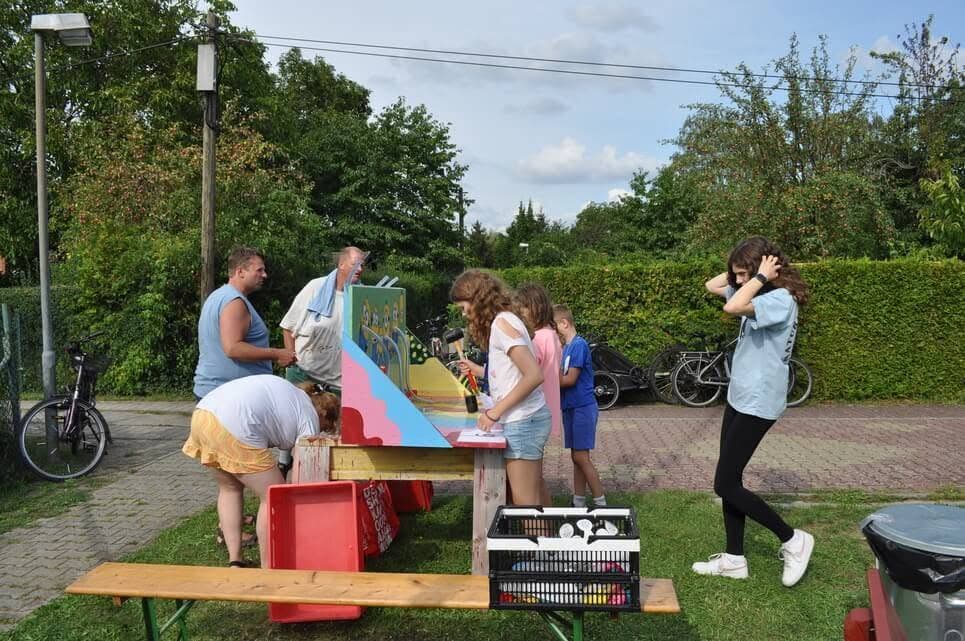 Erwachsene begleiten Kinder an einer rot gestrichenen Holzspielstation.