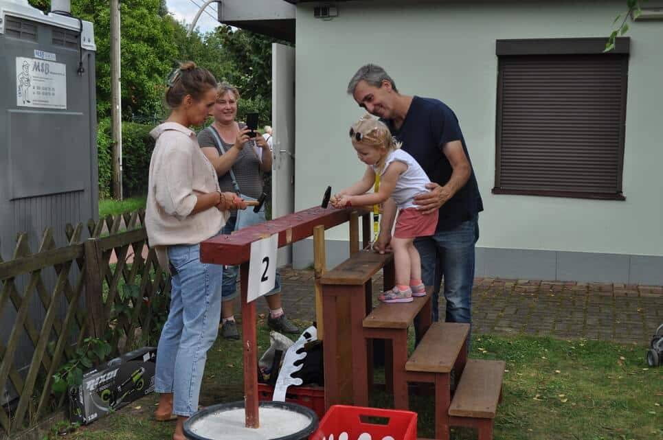 Eine Familie steht mit einem Kleinkind an der hölzernen Spielstation.