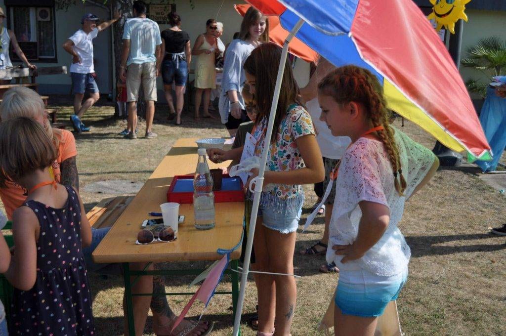 Mehrere Kinder stehen an einem Basteltisch unter einem Sonnenschirm.