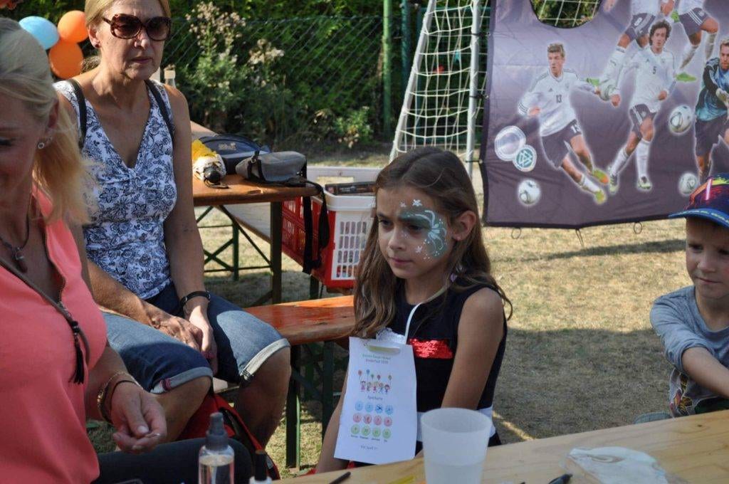 Ein Kind mit blau-weißer Gesichtsbemalung sitzt am Festtisch.