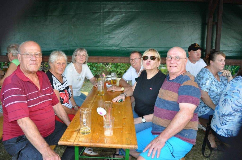 Eine größere Gruppe sitzt mit Getränken an einem langen Holztisch.