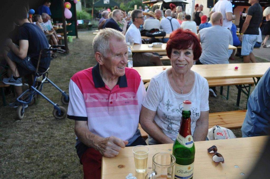 Zwei Gäste sitzen mit Getränken an einem Tisch auf dem Festgelände.