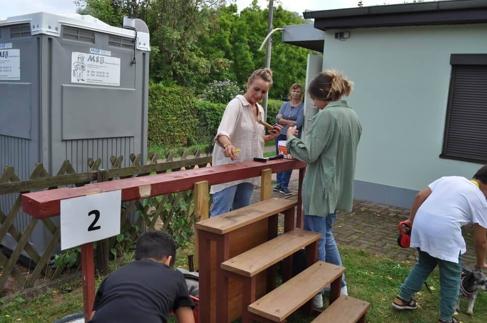 Kinderfest im Kleingartenverein Mehrere Helfer richten eine Spielstation aus Holzbänken ein.