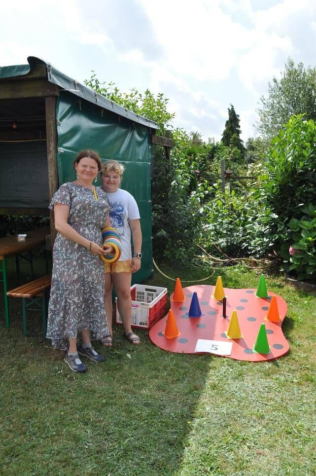 Kinderfest im Kleingartenverein Zwei Helferinnen stehen hinter einem bunten Kegelspiel auf dem Rasen.