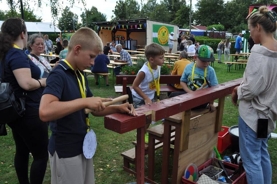 Kinderfest im Kleingartenverein Kinder und eine Helferin stehen an der langen Holzspielstation.
