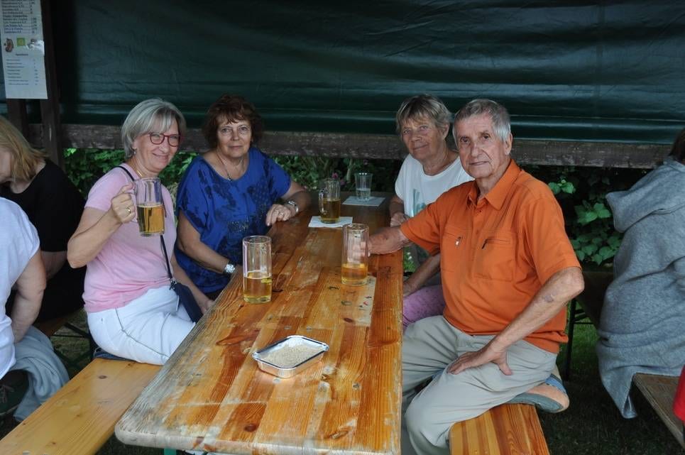 Unser Sommerfest 2023 Vier Gäste sitzen mit Getränken an einem Holztisch.