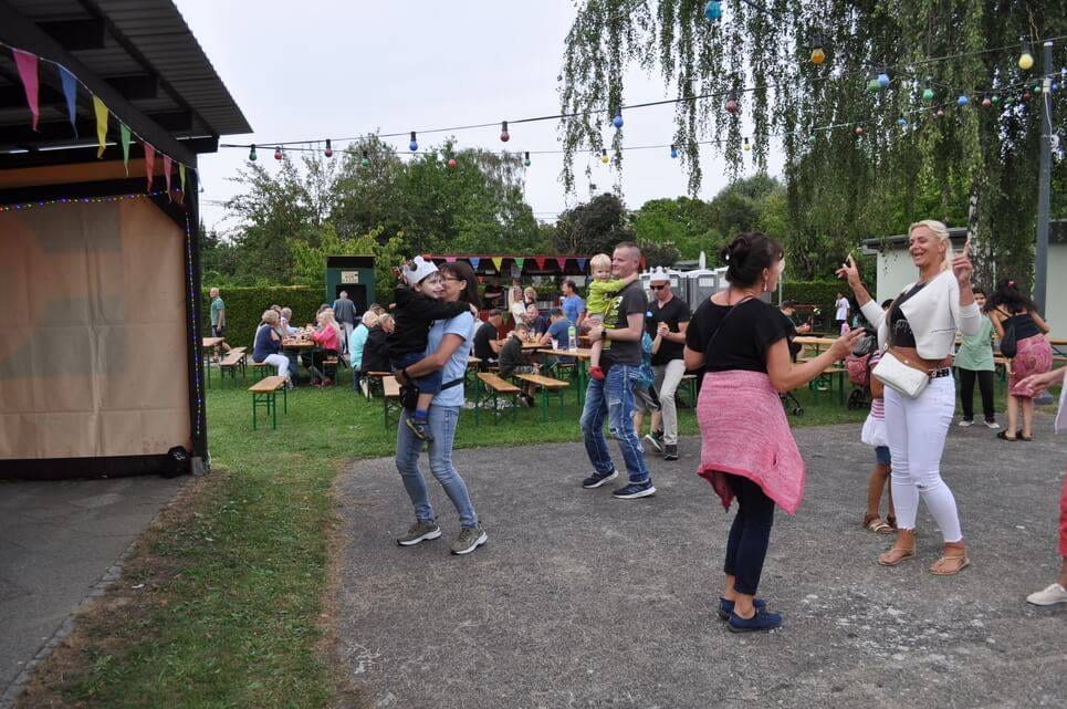 Unser Sommerfest 2023 Mehrere Paare tanzen vor den Sitzbänken am Vereinsheim.