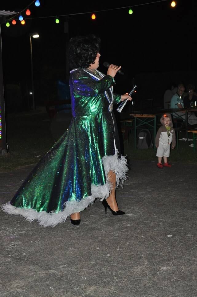 Unser Sommerfest 2023 Eine Künstlerin dreht sich in einem langen grünen Federkleid.
