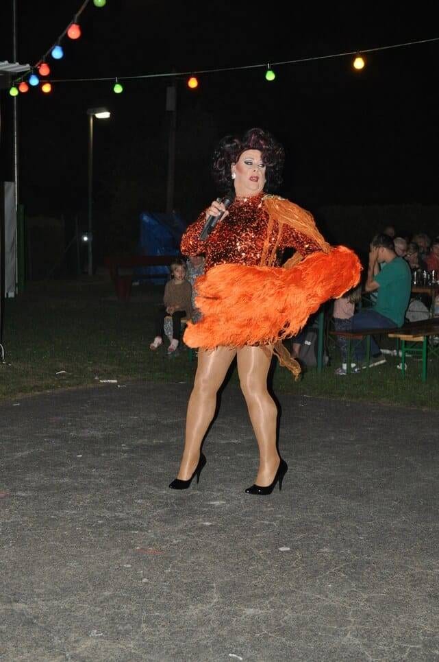 Unser Sommerfest 2023 Eine Künstlerin tritt in einem Kleid mit orangefarbenem Federschmuck auf.